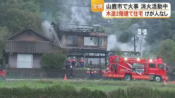山鹿市菊鹿町の住宅火災で煙の上がる建物と消防活動を写したテレビ熊本の報道画像